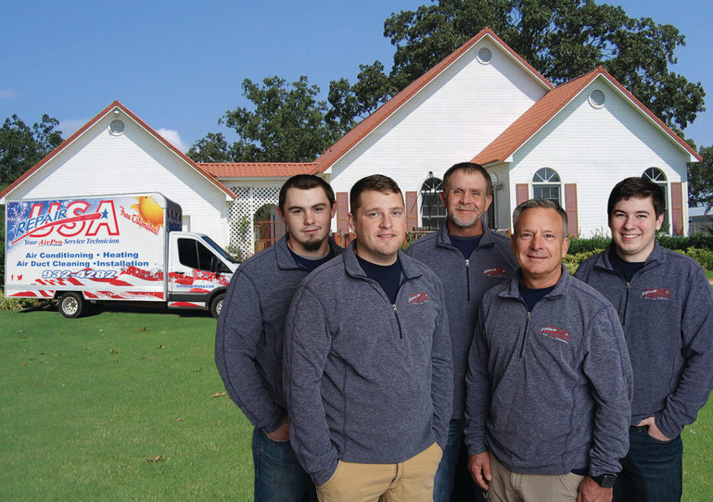 Team members of RepairUSA standing in front of a home with a branded truck in the back.