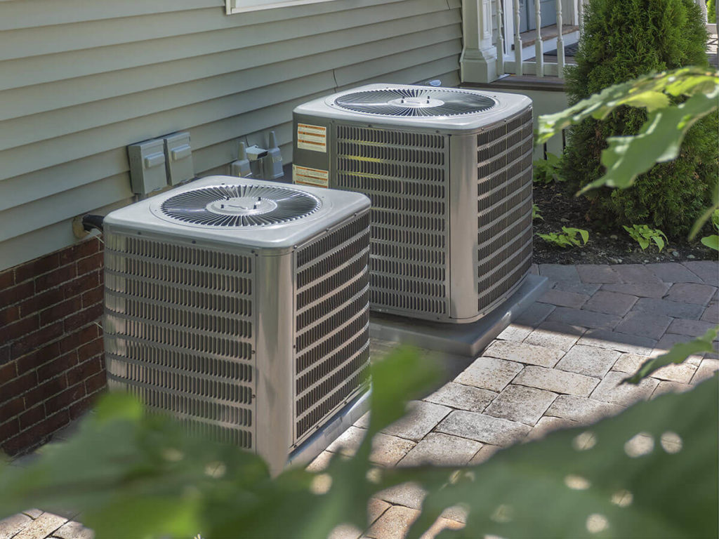 Two central air conditioner units installed on concrete slabs outside a home.