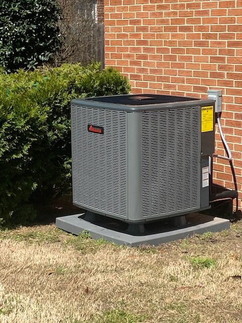 A central air conditioner unit installed outside of a brick home.