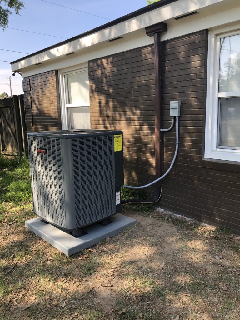 A central air conditioner condenser installed outside a one-story home.