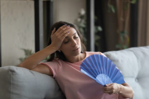 Young woman cooling herself with a hand fan as her room is extremely hot